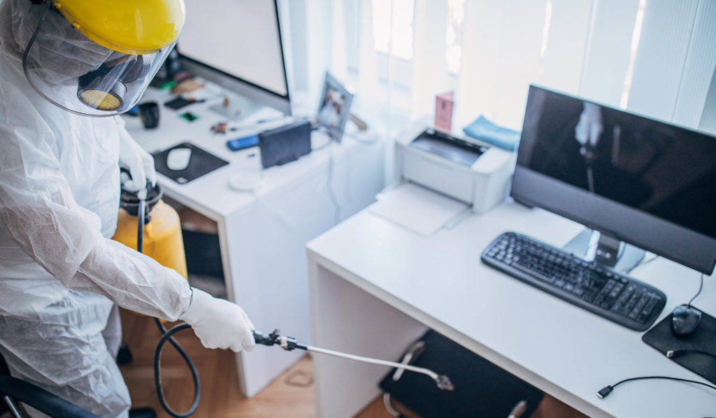 Horizon worker in protective suit disinfecting office work space. 